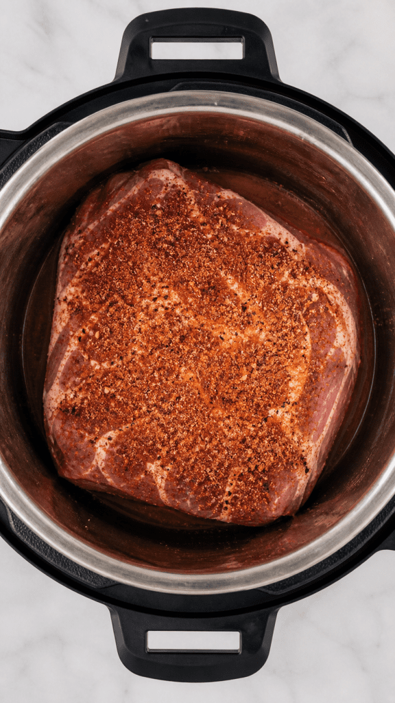 overhead shot of a pork shoulder in an instant pot with bbq seasoning sprinkled on top of it 