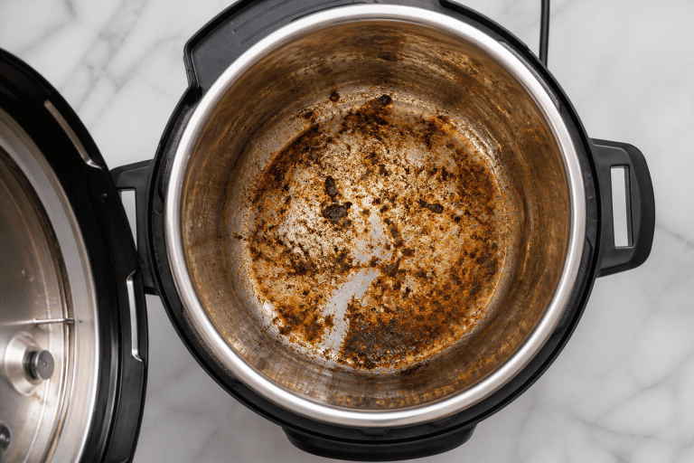 an open pressure cooker overhead with dried on food on the inside bowl